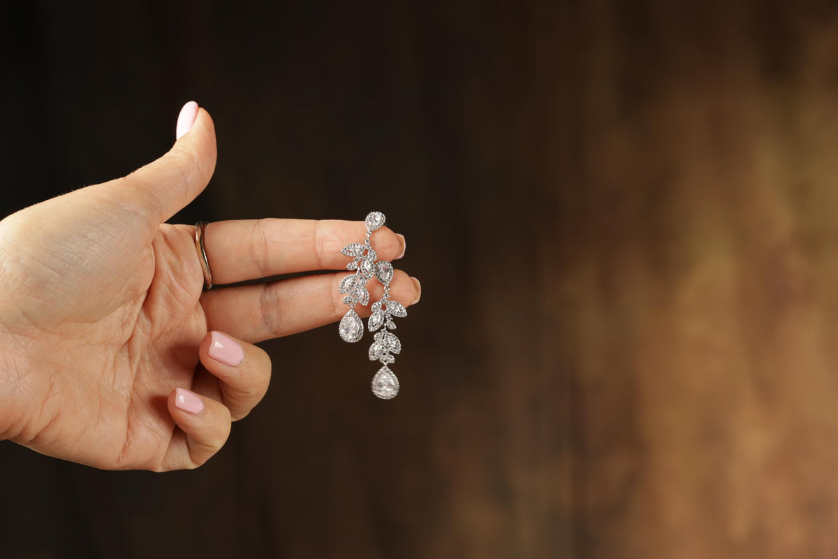 A hand holding a pair of diamond earrings against a blurred background.