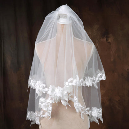 A white wedding veil with delicate white lace trim is displayed on a mannequin against a dark background.