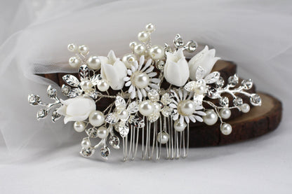 A decorative hair clip adorned with white flowers and pearls rests on a wooden surface.