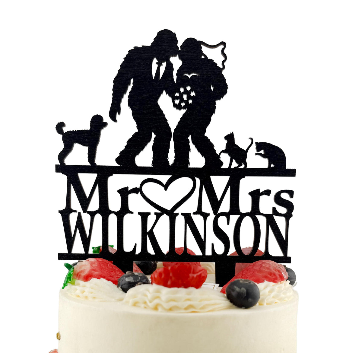 A black silhouette of a bride and groom on top of a cake, with the words "Mr. Wilton" written below them.