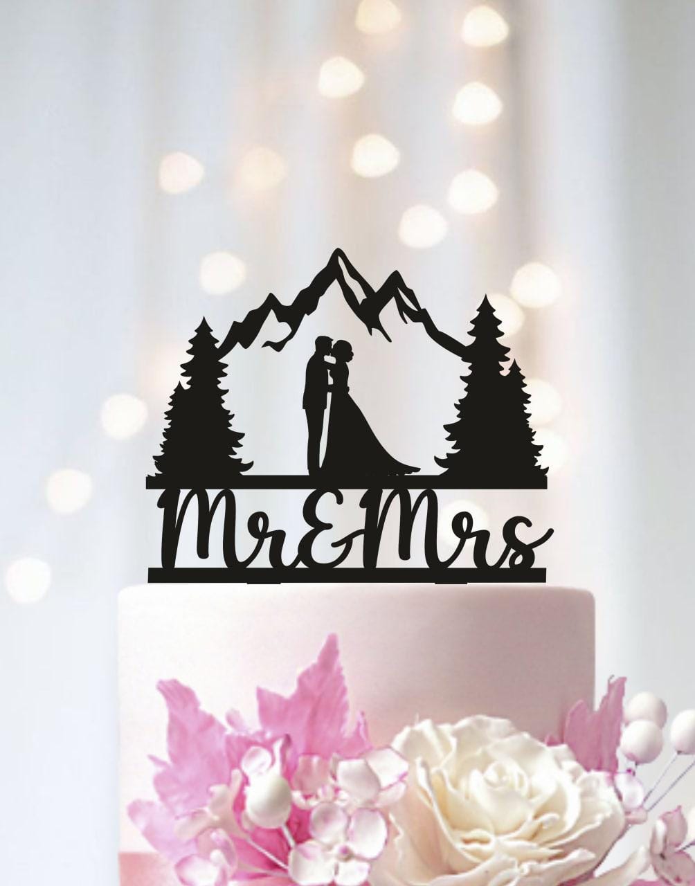 A black silhouette of a bride and groom on a cake topper, with mountains in the background, and the words "Mr & Mrs" written below.