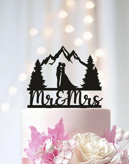 A black silhouette of a bride and groom on a cake topper, with mountains in the background, and the words "Mr & Mrs" written below.