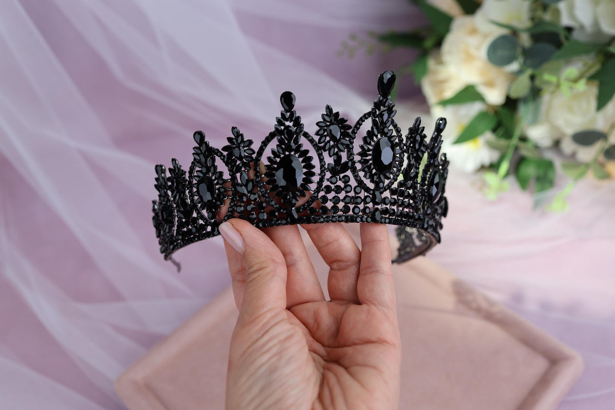 a hand holding a tiara in front of a bouquet of flowers