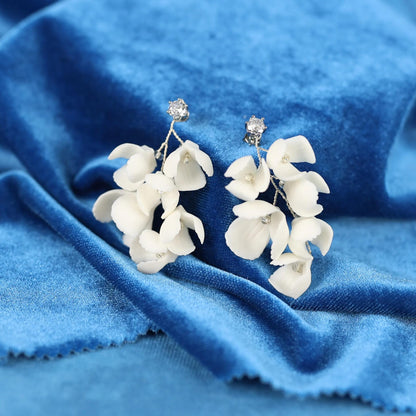 A pair of white flower-shaped earrings with small diamonds on top, resting on a blue fabric surface.