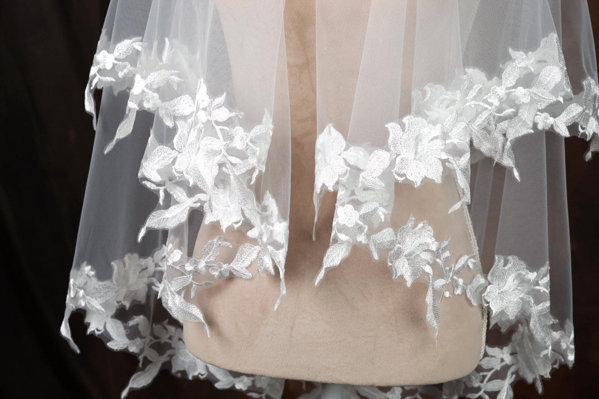 A close-up view of a delicate white lace veil with intricate floral embroidery, displayed on a mannequin or model.