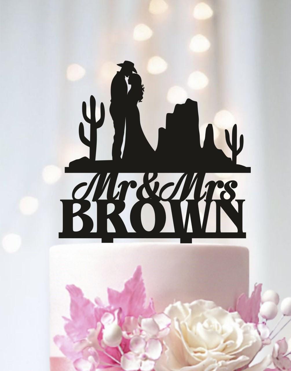A black silhouette of a couple embracing, with the text "Mr & Mrs Brown" above them, on a wedding cake topper.