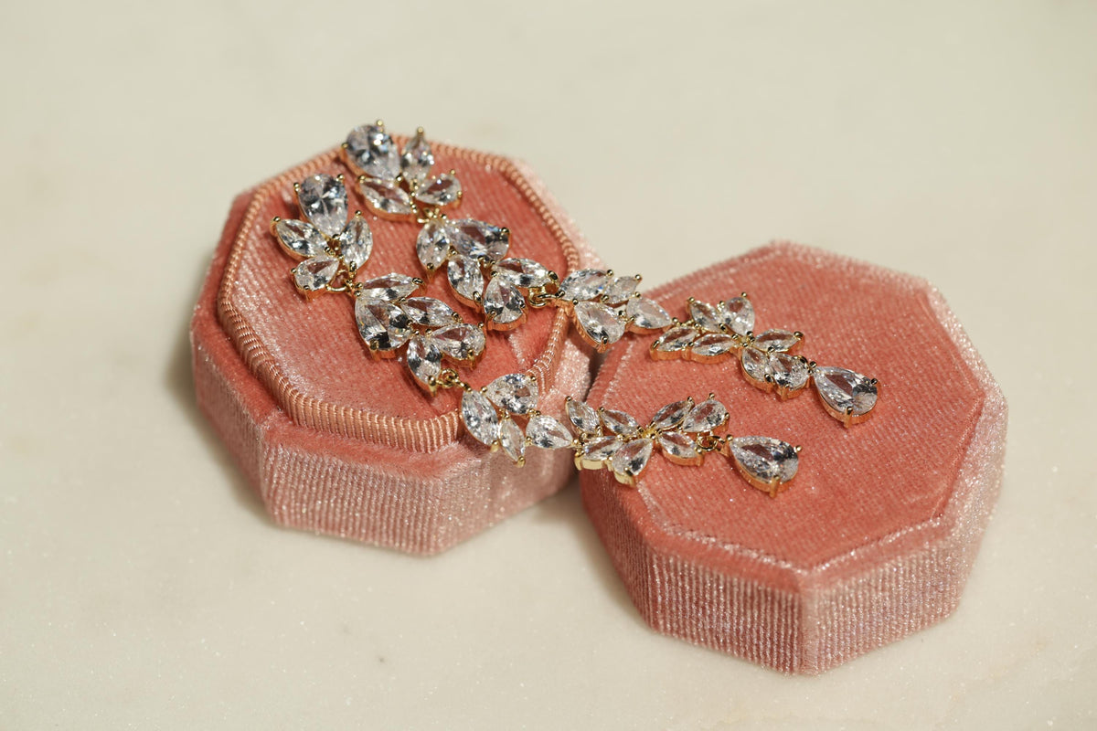 A pair of diamond earrings in a pink velvet jewelry box, with the earrings hanging from the box.