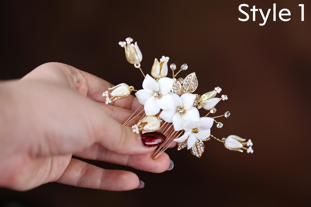 A hand holding a decorative hair clip with white flowers and gold accents.