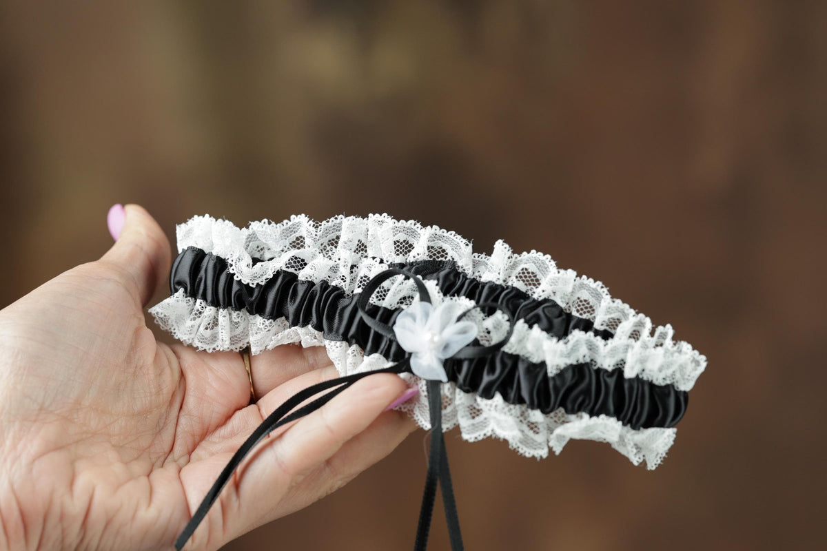 A hand holding a black and white lace garter belt with a white flower decoration.