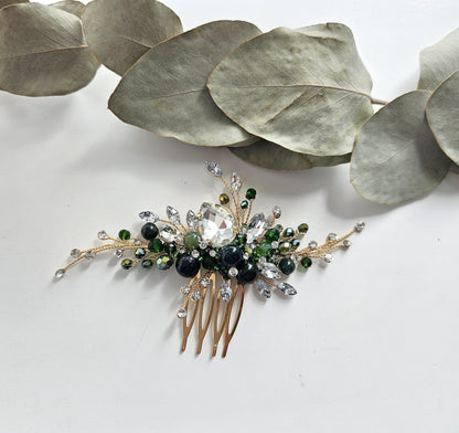 A decorative hair accessory with a gold-colored comb and a large crystal or gemstone at the center, surrounded by smaller stones and leaves.