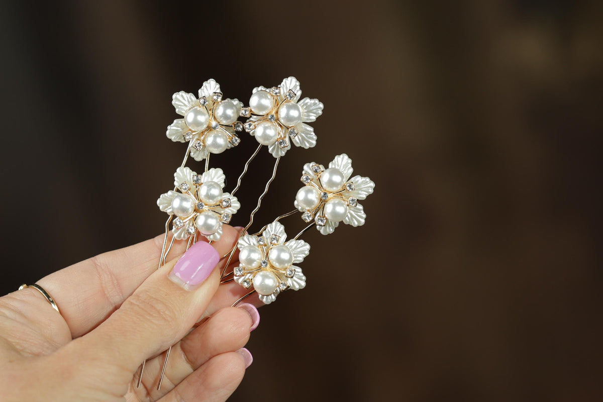 A hand holding a group of ornate hair clips with white pearls and gold accents.