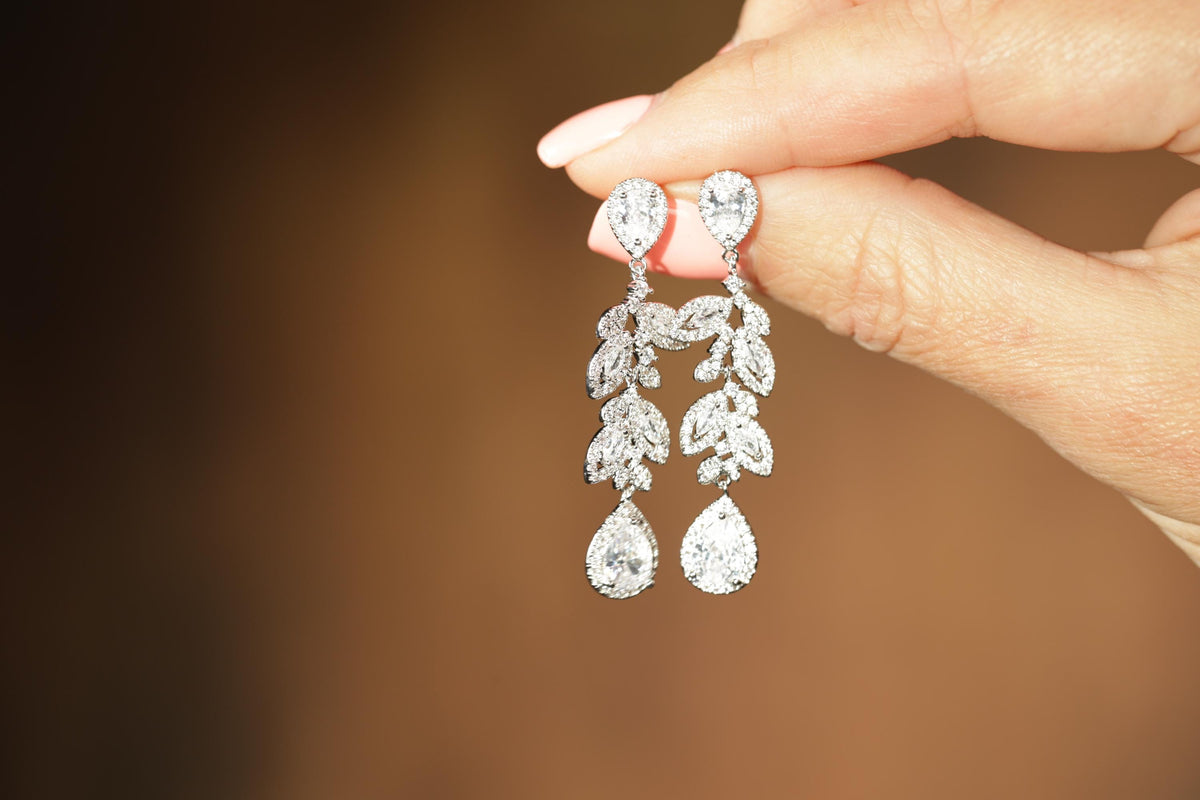 A hand holding a pair of elegant diamond earrings with intricate leaf designs.