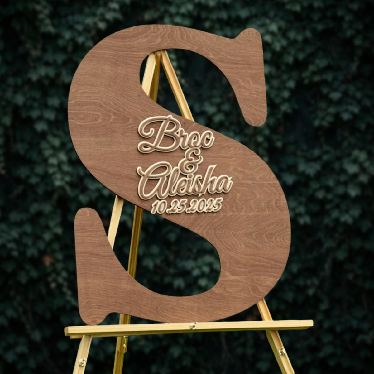 A wooden sign with the letters 'S' and 'A' in the center, displaying the names 'Bree & Alisha' and the date '10.25.2025' on it.