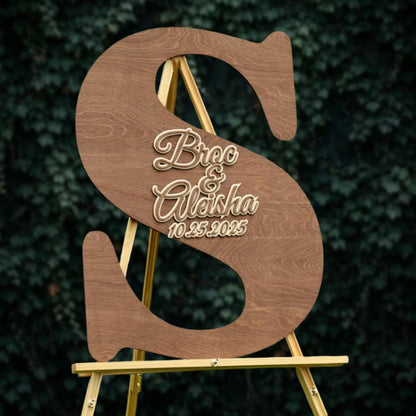 A wooden sign with the letters 'S' and 'A' in the center, displaying the names 'Bree & Alisha' and the date '10.25.2025' on it.