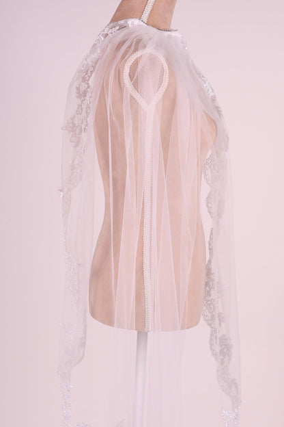 A mannequin wearing a white lace veil with a heart-shaped clasp.