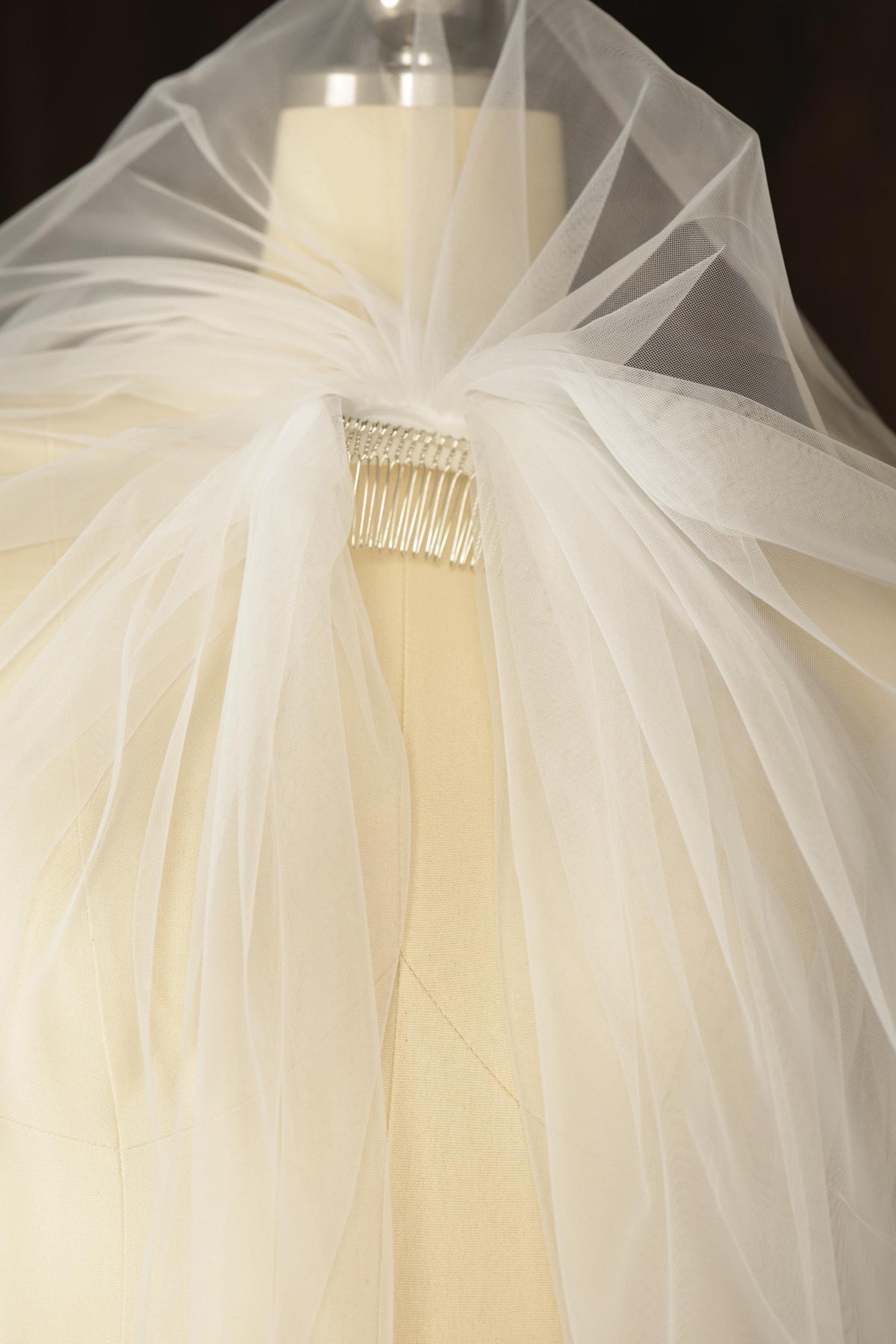 A close-up view of a delicate white veil with a beaded clasp, showcasing the intricate details and soft texture of the fabric.