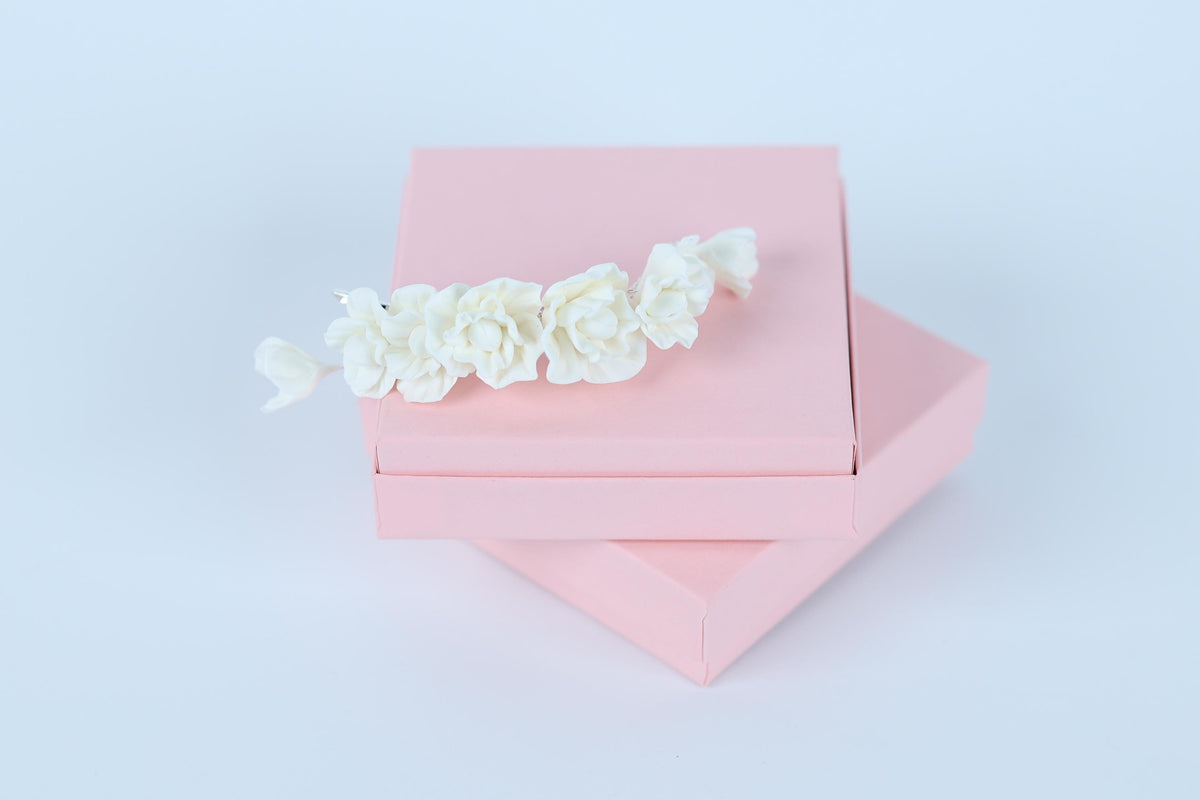 A pink box with a delicate white flower arrangement on top, set against a plain white background.