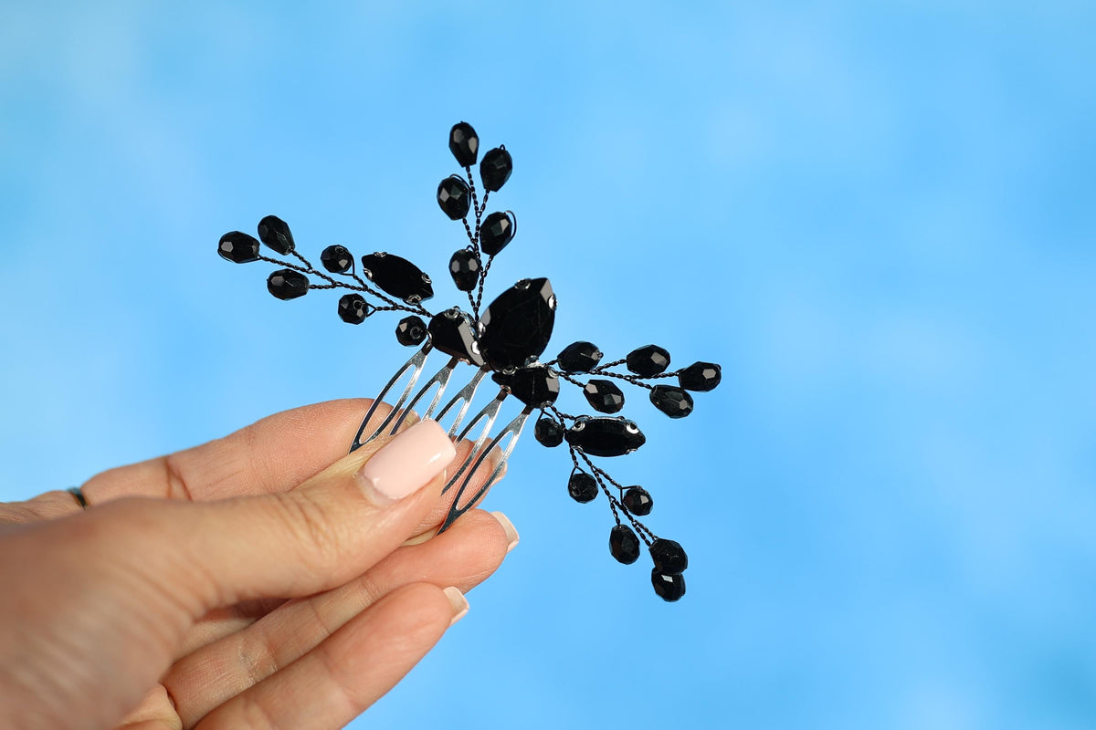 A hand holding a decorative hair accessory with black beads against a blue background.
