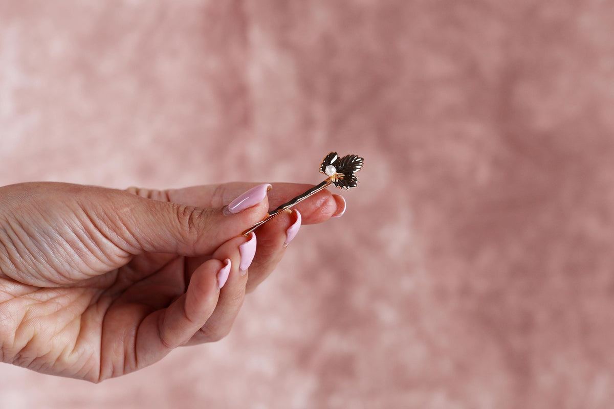 A hand holding a small, ornate pin or brooch with a floral design.
