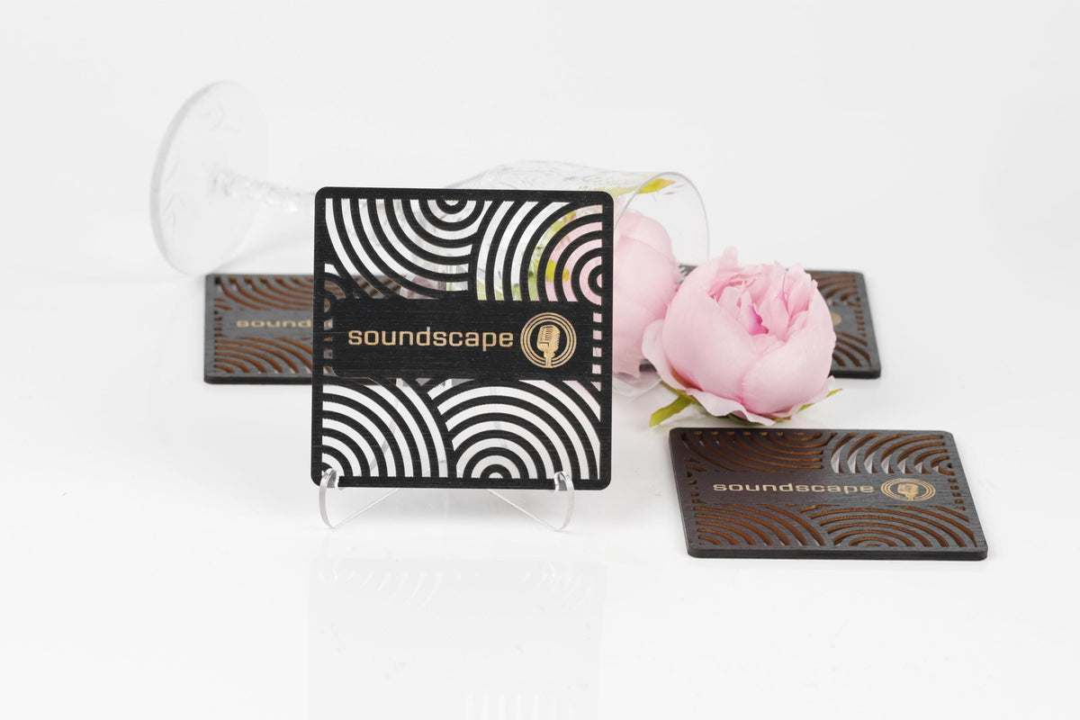 a business card stand with a black and white striped design, a pink flower, and two coasters with the word "soundscape" printed on them.