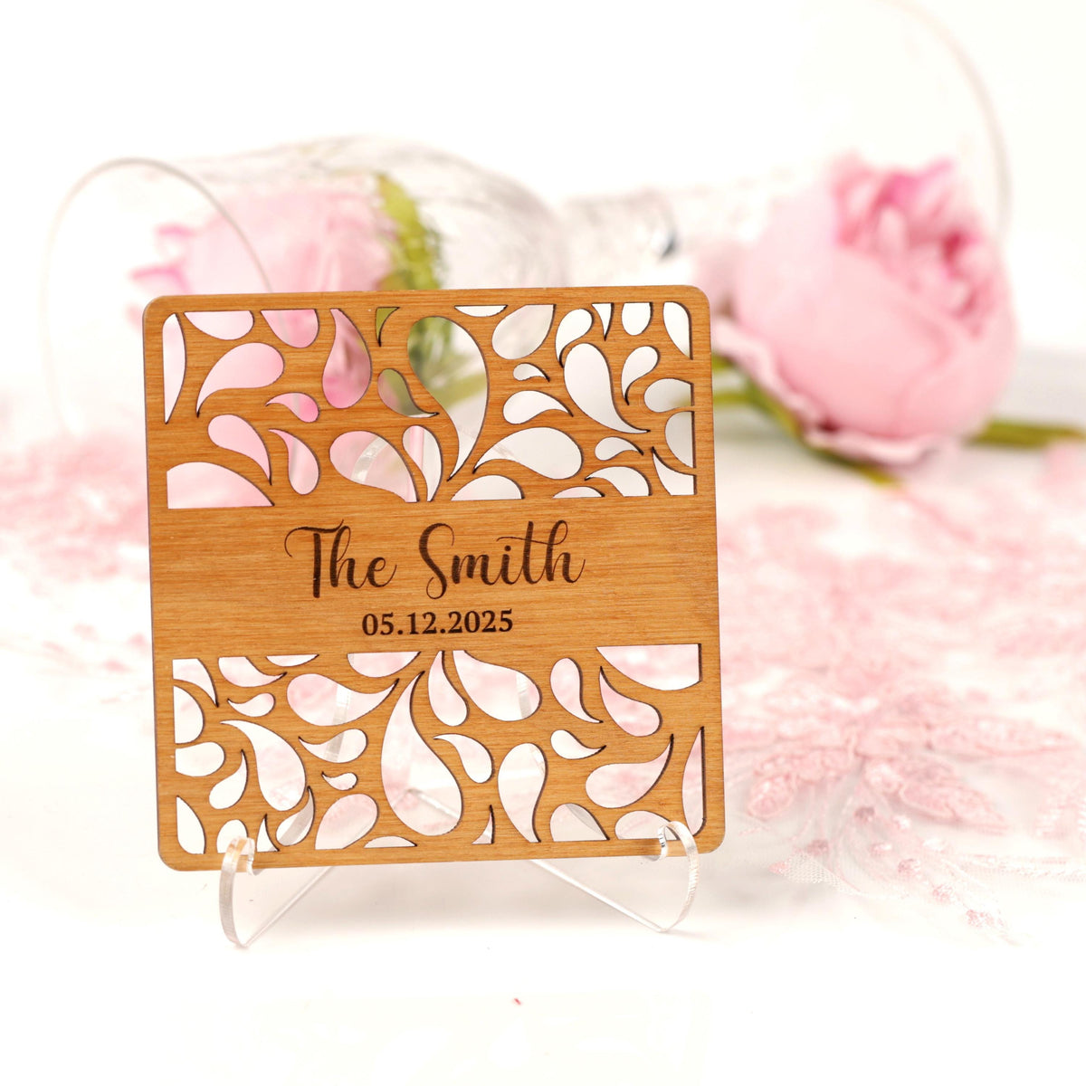 A wooden coaster with a floral design and the name "The Smith" printed on it, placed on a white surface with a pink rose in the background.