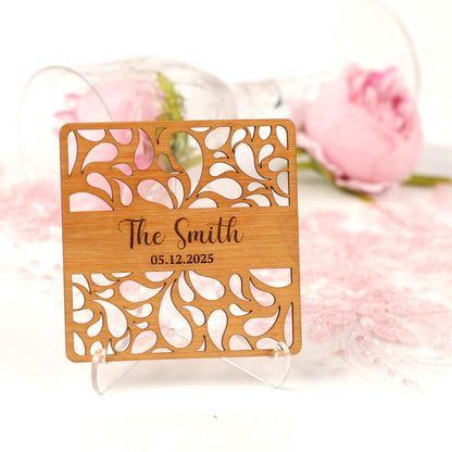 A wooden coaster with a floral design and the name "The Smith" printed on it, placed on a white surface with a pink rose in the background.