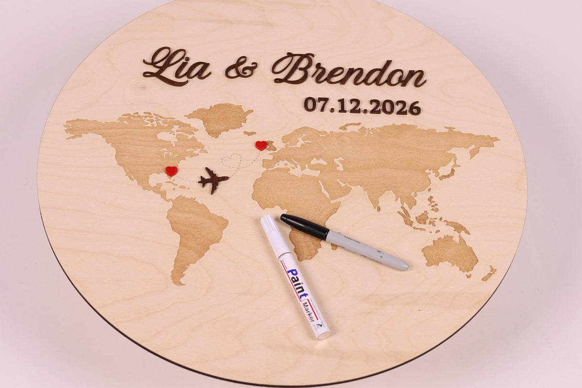 A wooden plaque with a world map and the names 'Lia & Brandon' written on it. A marker is placed on the plaque, and there is a small airplane and a heart shape on the map.