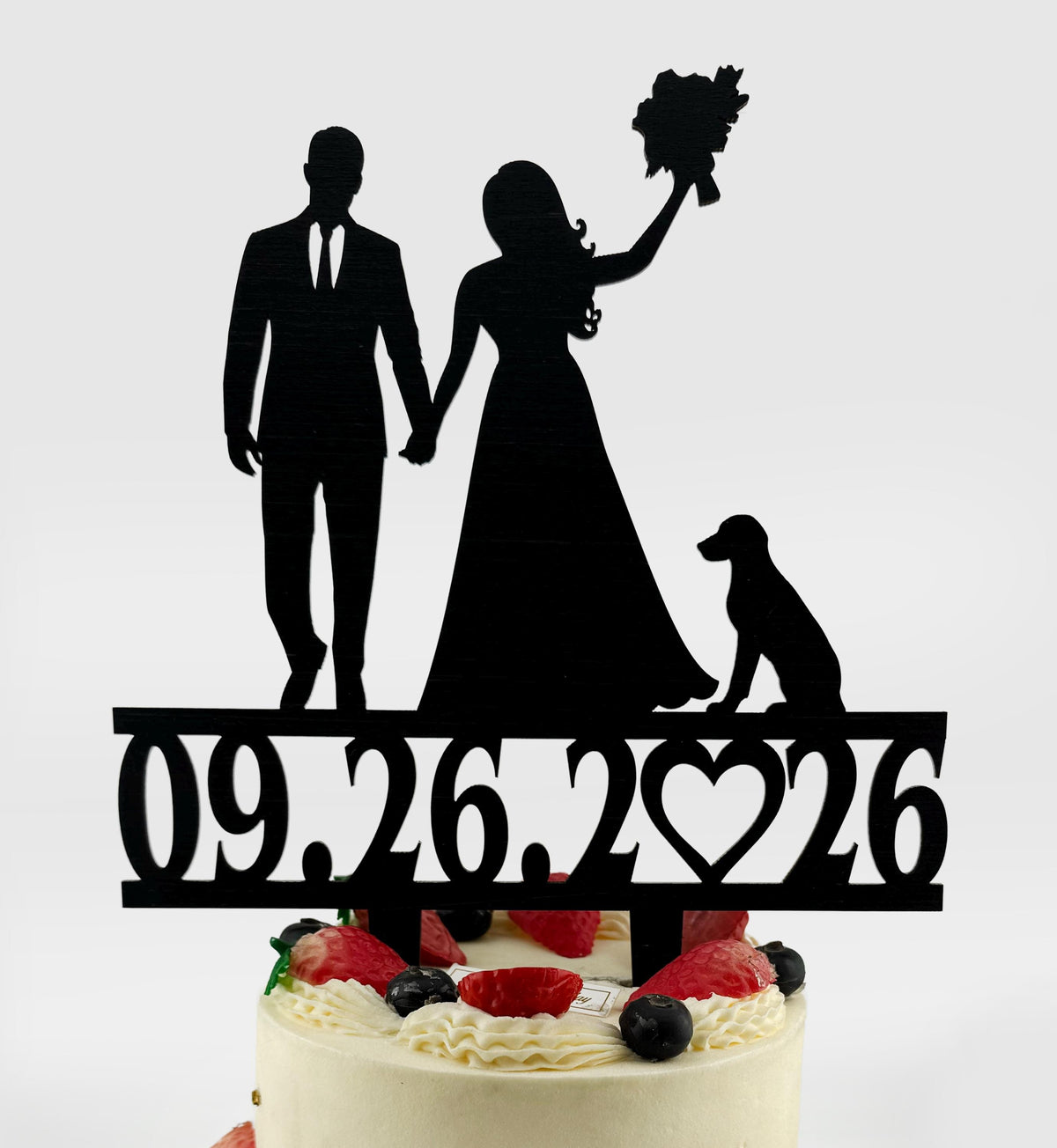 A silhouette of a bride and groom holding hands, with a dog and a heart-shaped number on a cake topper.