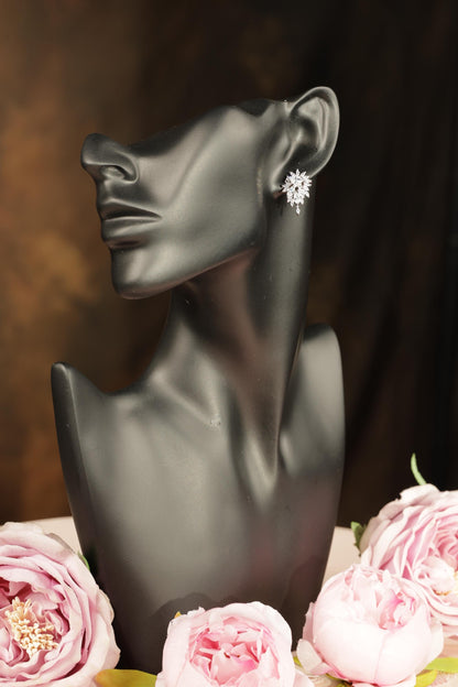 A black bust form with a pair of earrings on it, placed next to a bouquet of pink roses.