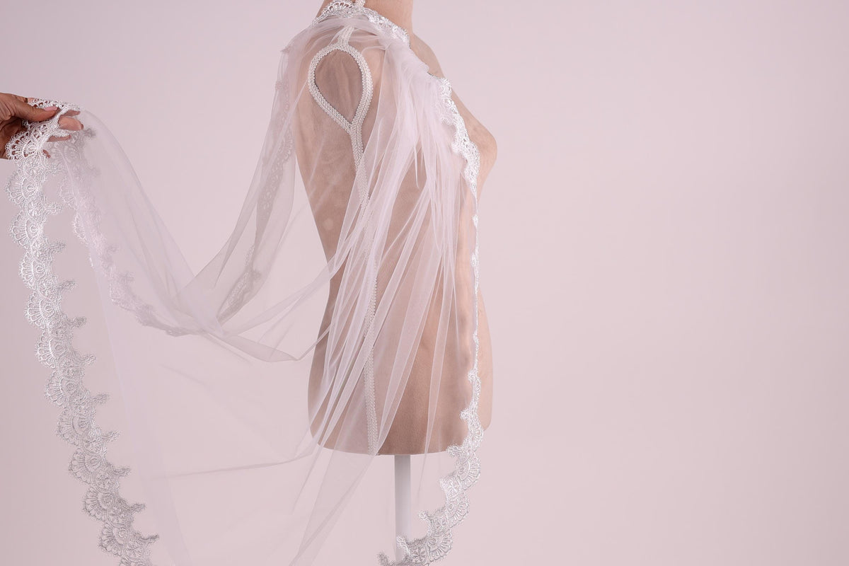 A mannequin wearing a white lace veil with a delicate, intricate design.
