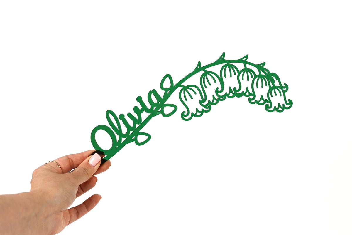 A hand holding a green paper cutout of a lily of the valley flower.