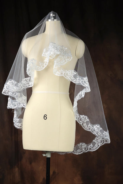 A white wedding veil with intricate lace detailing is displayed on a mannequin.