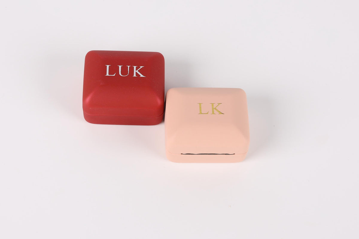 Two square jewelry boxes, one red and one pink, with the letters "LUK" and "LK" printed on them.