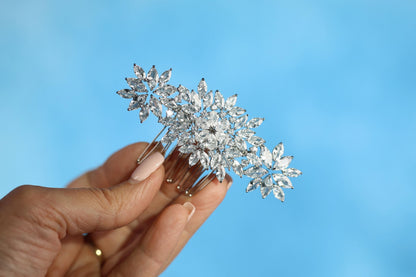 A hand holding a decorative hair accessory with multiple small, sparkling crystal elements against a bright blue background.