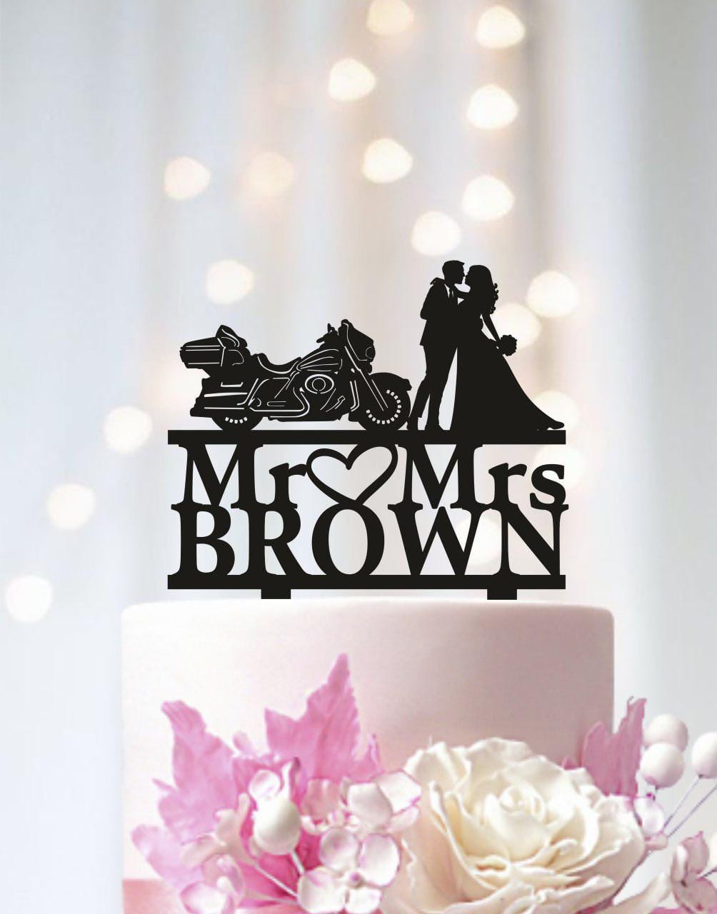 A black silhouette of a couple embracing a motorcycle on a cake topper, with the text "Mr. Brown" below it.