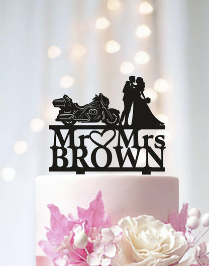 A black silhouette of a couple embracing a motorcycle on a cake topper, with the text "Mr. Brown" below it.
