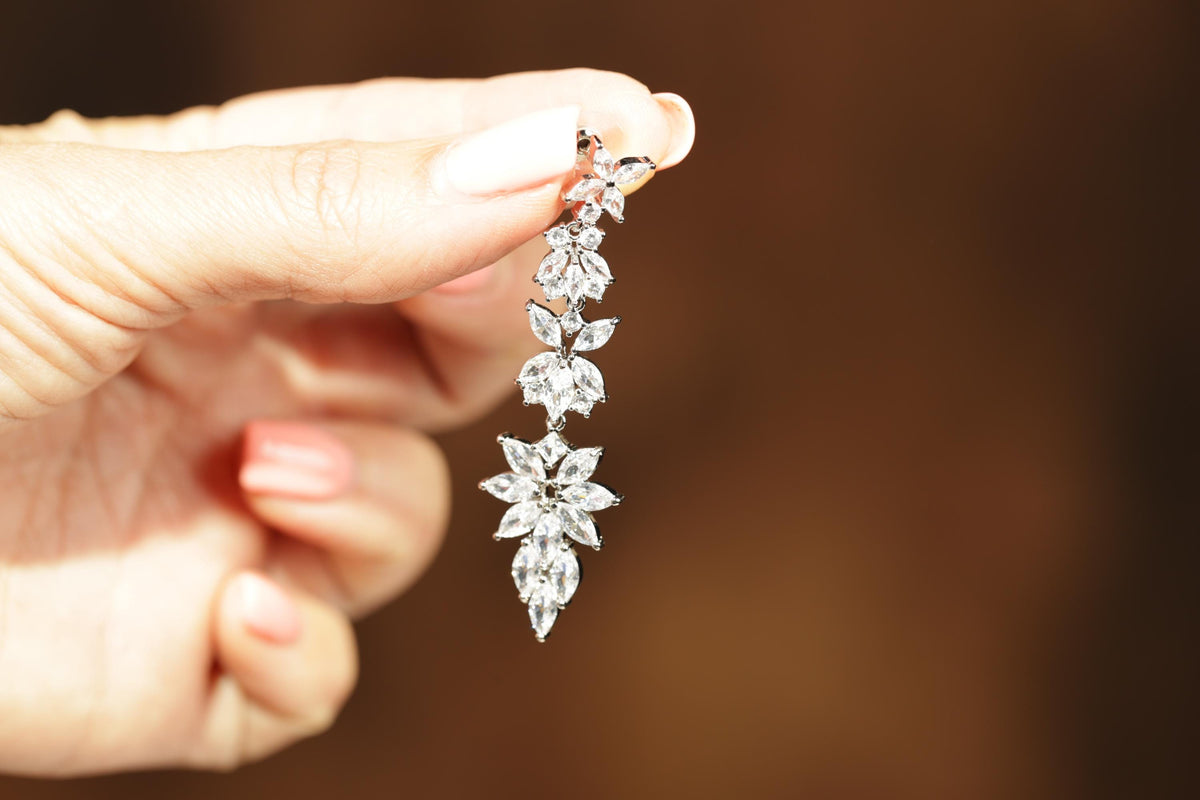 A close-up of a person's hand holding a delicate, sparkling diamond earring.