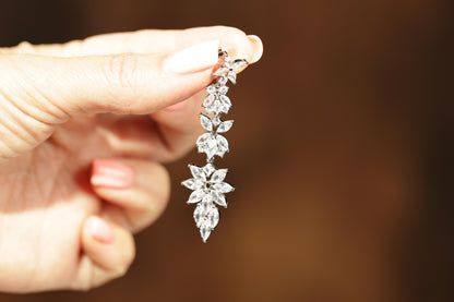 A close-up of a person's hand holding a delicate, sparkling diamond earring.