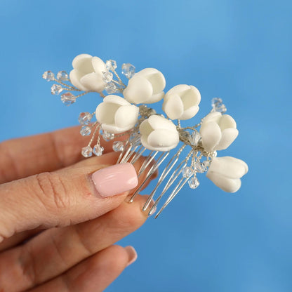 A hand holding a decorative hair clip with white flower-shaped elements against a blue background.