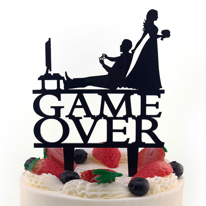 A silhouette of a bride and groom playing a video game on a cake topper with the text "GAME OVER".