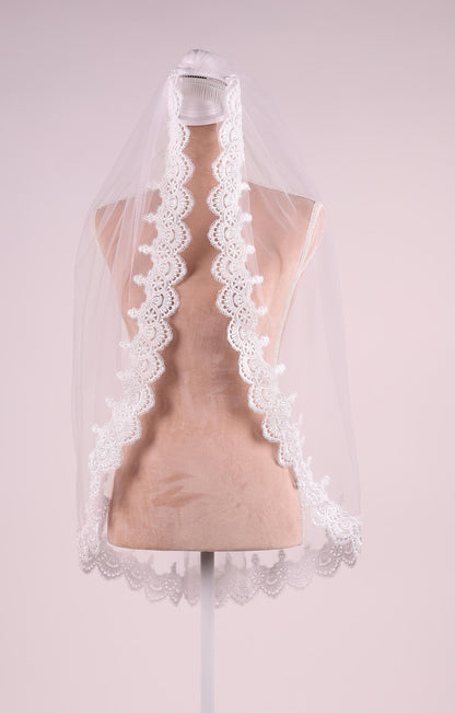 A mannequin wearing a white lace veil with a scalloped edge.