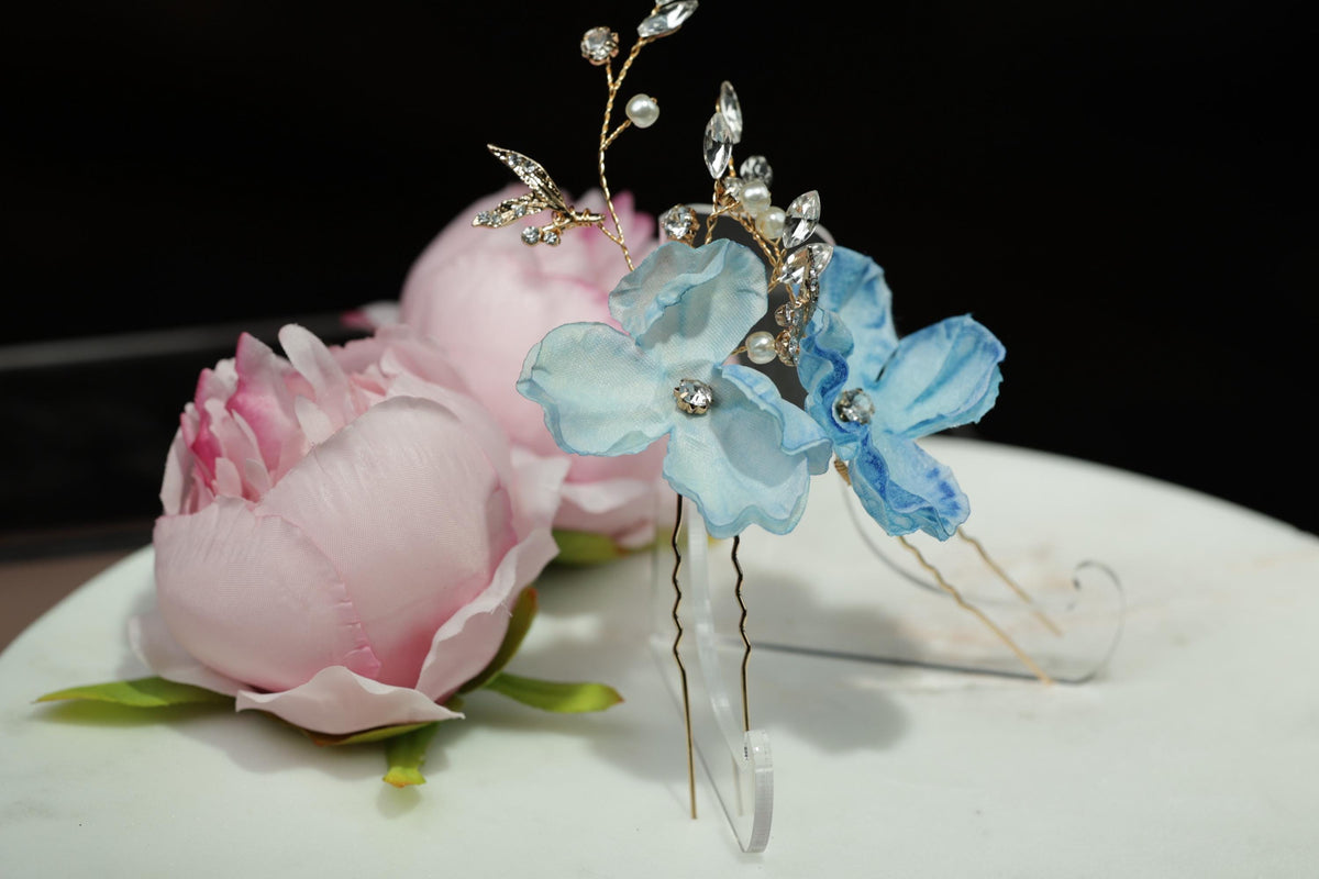 a close-up view of a decorative floral arrangement, including a pink peony and a blue flower, with a clear vase holding the flowers.