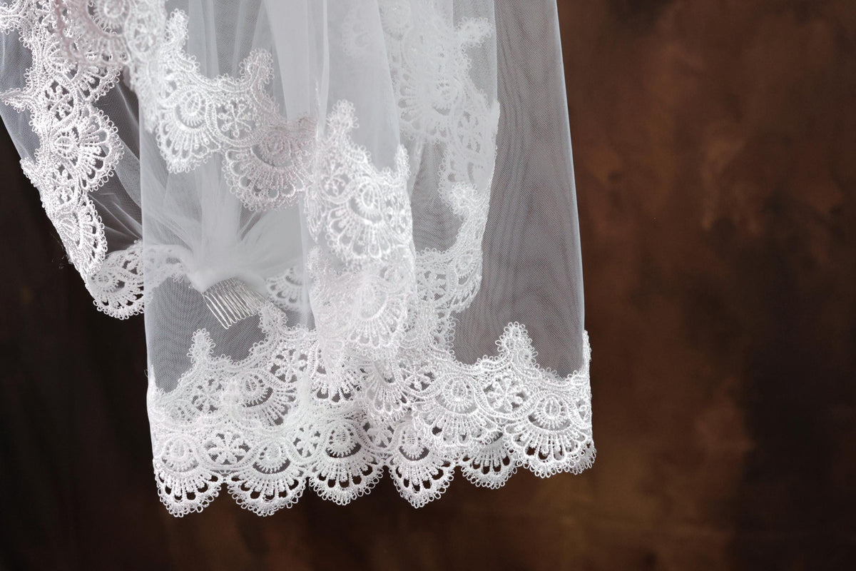 A close-up view of a delicate white lace veil with intricate lace patterns, hanging against a dark background.