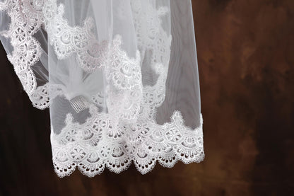A close-up view of a delicate white lace veil with intricate lace patterns, hanging against a dark background.
