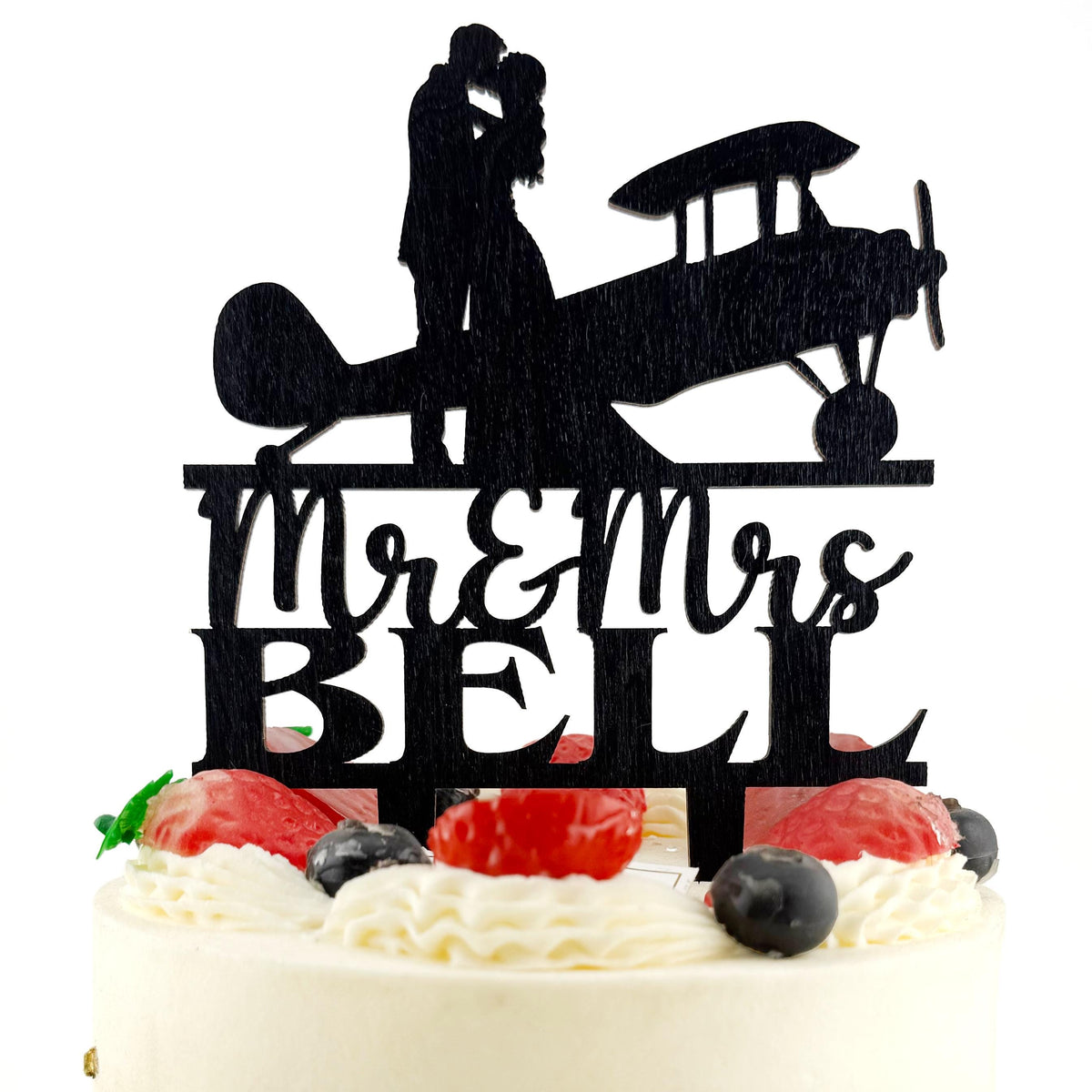 A silhouette of a couple embracing an airplane on a cake topper, with the words "Mr & Mrs Bell" written below.