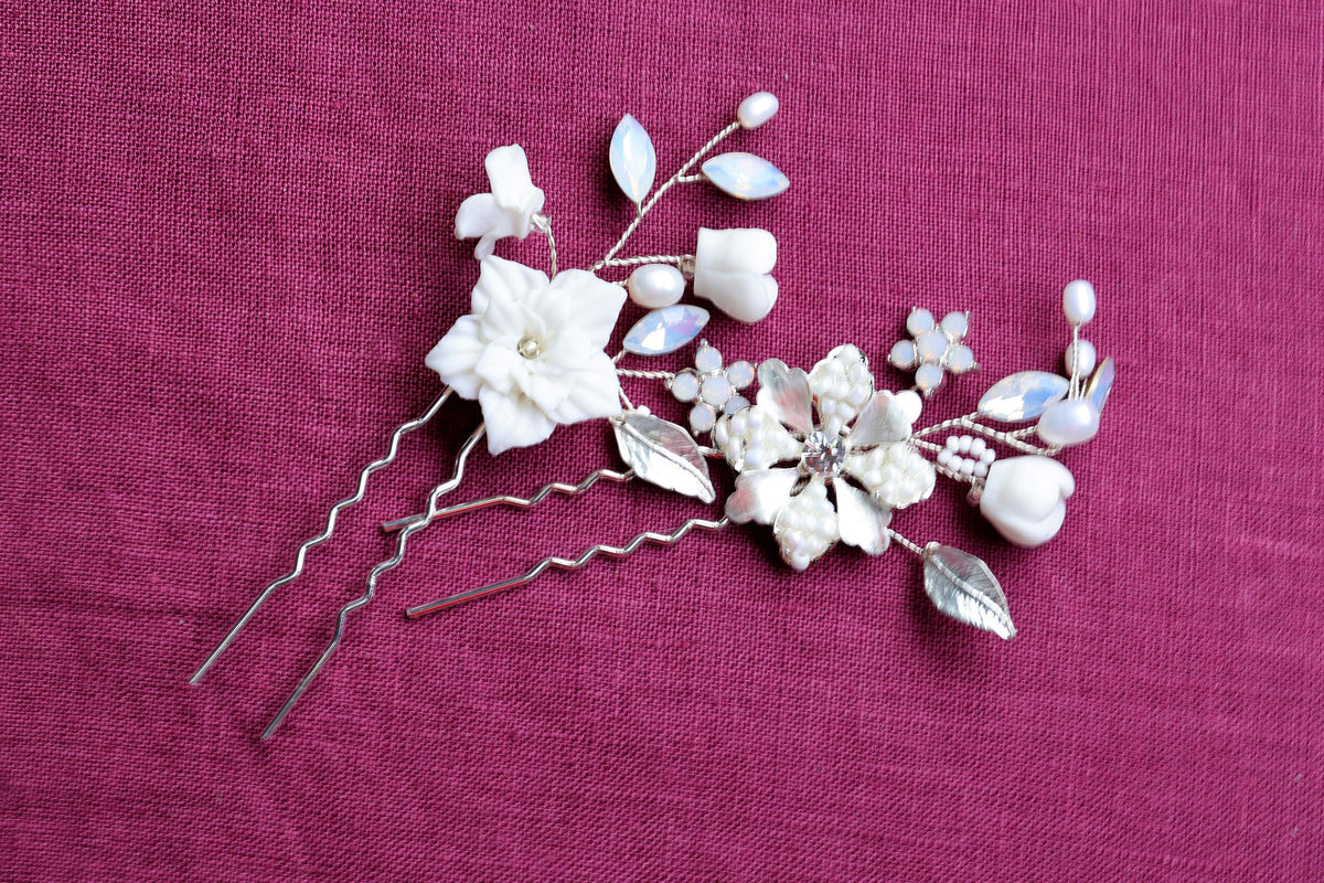 A decorative hair clip with white flowers and silver metal elements rests on a red fabric background.