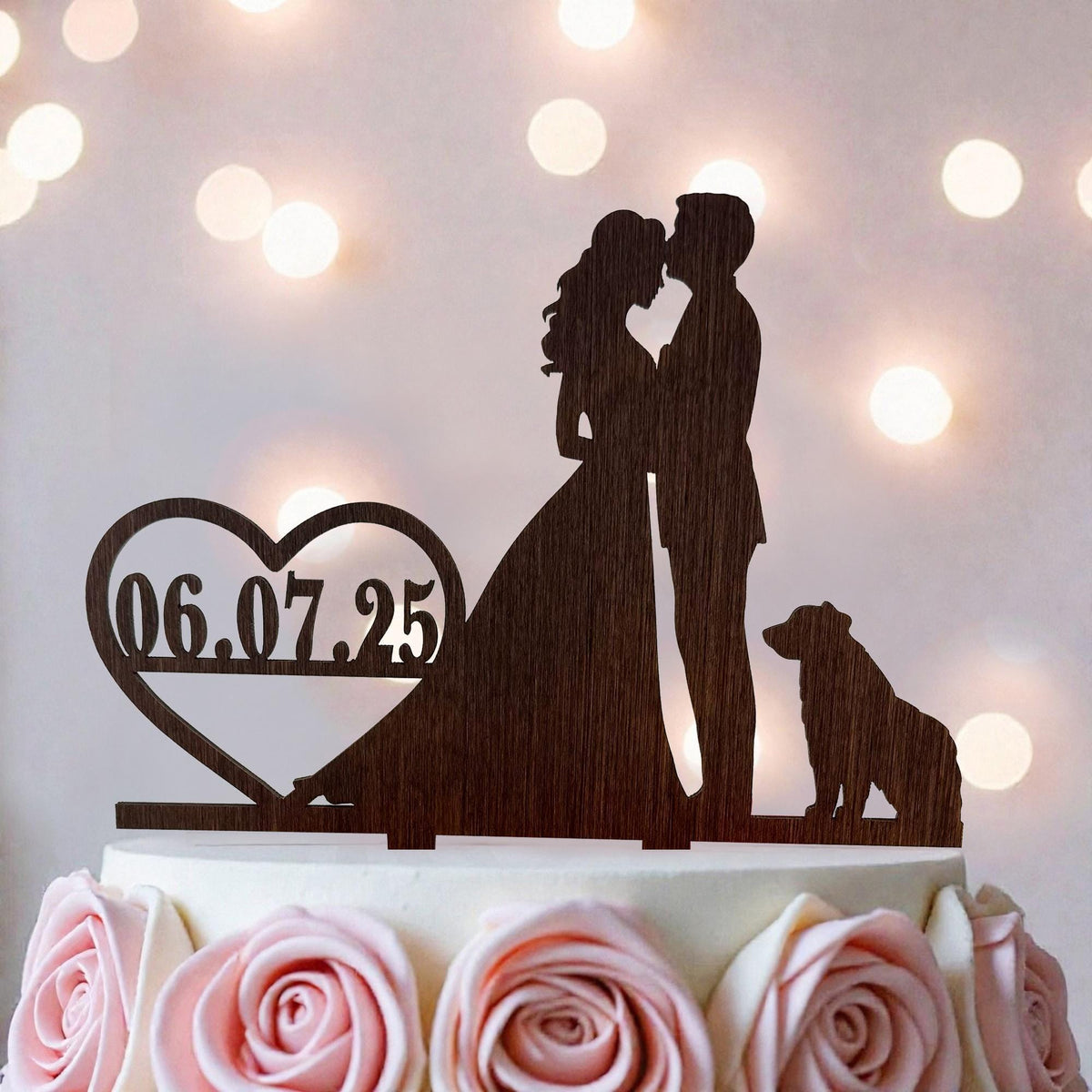 A wooden silhouette of a bride and groom kissing on a cake topper, with a heart-shaped date display below.