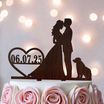 A wooden silhouette of a bride and groom kissing on a cake topper, with a heart-shaped date display below.